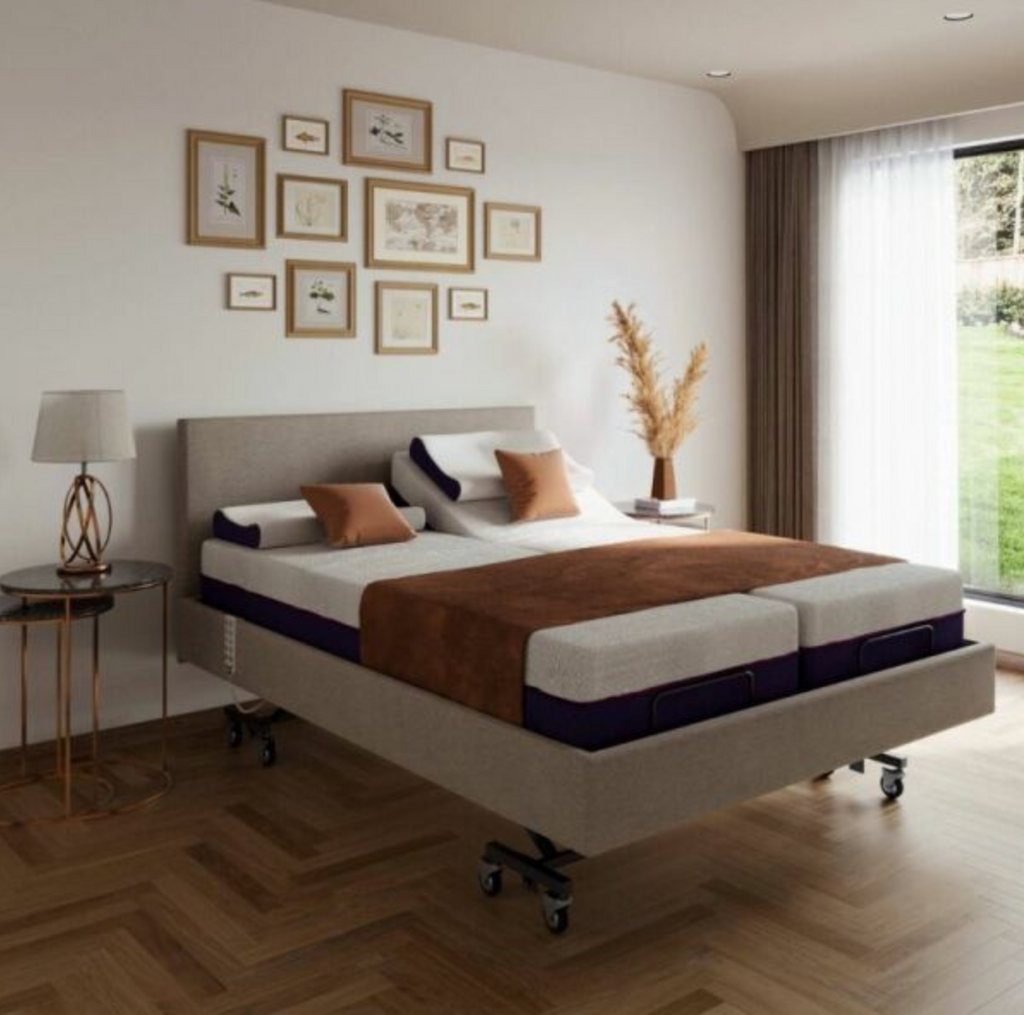 A high-end adjustable platform bed with a light beige upholstered frame and black caster wheels, styled in a modern bedroom with a herringbone wood floor, wall art, and a window with sheer curtains.