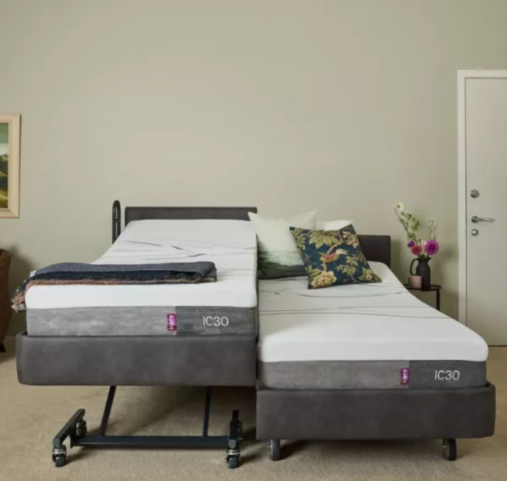 Two adjustable bed frames with mattresses, shown side by side in a bedroom setting. The beds have dark gray upholstered bases and frames with white mattresses.