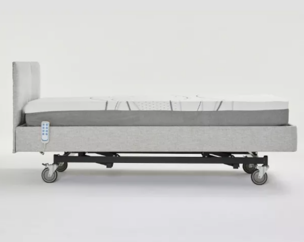 An electric hospital bed with a light gray upholstered frame, a white mattress, and a black wheeled base, shown from a side profile against a white studio background.