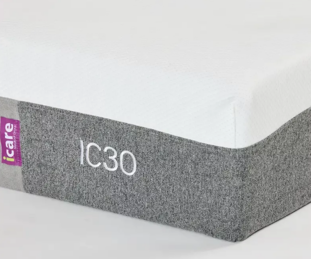 Close-up of the side of a mattress showing a white top surface, a gray textured side skirt with the model name 'IC30' in white text, and a small purple 'iCare' brand tag.
